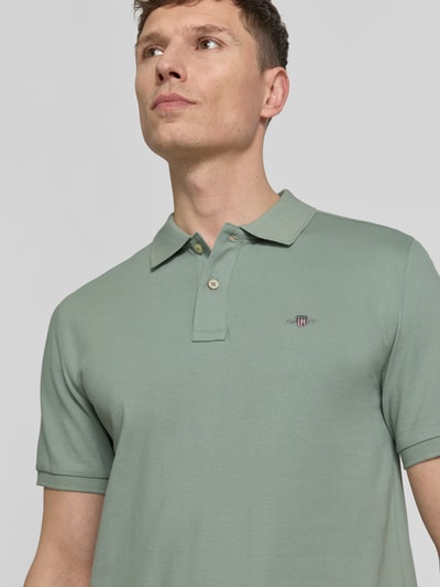 Mężczyzna nosi Slim Fit Poloshirt mit Logo-Stitching od Gant z bawełny, kołnierzykiem polo, krótki rękaw, wyhaftowane logo, z przodu, zbliżenie na górną część ciała