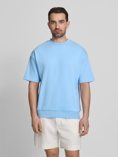 Männermodel trägt Oversized T-Shirt mit Rundhalsausschnitt von Lindbergh aus Baumwoll-Mix in Hellblau mit Label-Detail, Rückenlänge 70 cm, Ganzkörperansicht von vorne.