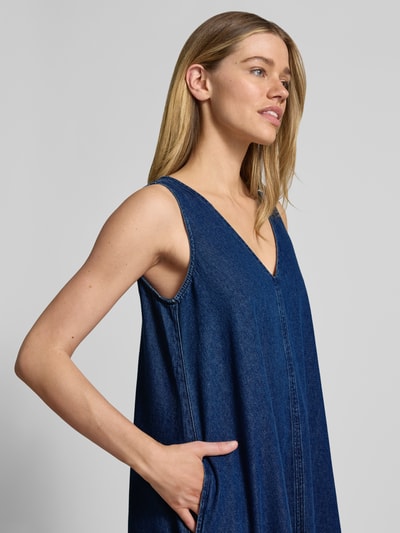 Vrouwenmodel draagt Loose fit Jeanskleid aus Baumwoll-Lyocell-Mix van Armedangels in denimlook, brede bandjes, V-hals, steekzakken, twill materiaalverwerking, midilengte, labelpatch. Nahaufnahme bovenlichaam schuin van voren.
