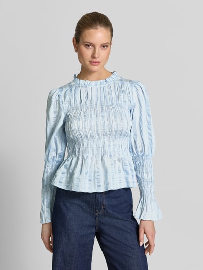 Frauenmodel trägt Bluse in tailliertem Schnitt mit Smok-Details Modell 'RAVA' von YAS, hellblau, strukturierte Oberfläche, Nahaufnahme Oberkörper. Viskose-Mix mit Lyocell-Anteil, Rückenlänge 54 cm, Ärmellänge 65 cm.