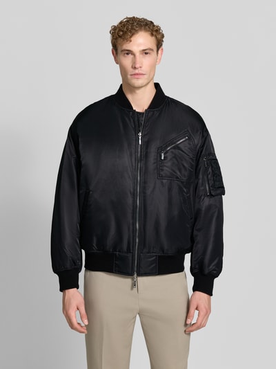 Männermodel trägt Bomberjacke mit Stretch-Anteil von Emporio Armani in Schwarz, Satin-Optik, lockere Passform, Ganzkörperansicht von vorne.
