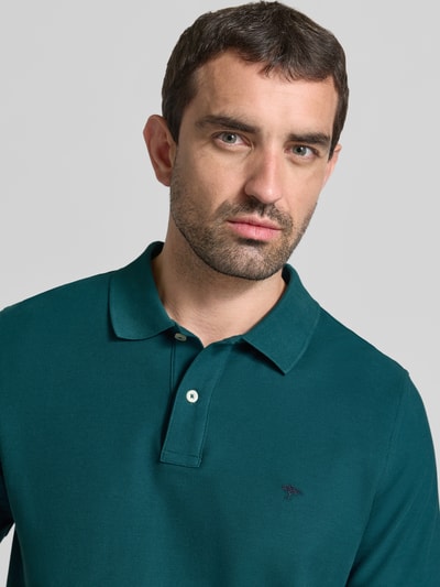 Männermodel trägt Regular Fit Poloshirt mit Label-Stitching von Fynch-Hatton in Dunkelgrün, reine Baumwolle, Knopfleiste, Nahaufnahme Oberkörper.