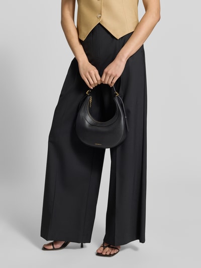 Frauenmodel trägt schwarze Shoulder Bag mit Strukturmuster Modell 'Whisper' von Coccinelle, Hauptfach mit Reißverschluss, Nahaufnahme Oberkörper.