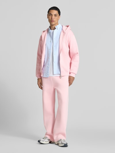 Männermodel trägt Sweatjacke aus Baumwoll-Mix von REVIEW in Rosa mit lockerer Passform und Kängurutasche, Ganzkörperansicht von vorne.