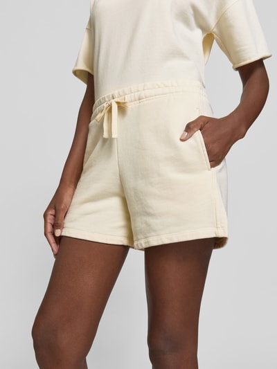 Frauenmodel trägt Shorts mit Modal-Anteil von Juvia in Creme, Baumwoll-Mix mit Modal-Anteil, Regular-Fit, Eingrifftaschen, elastischer Bund mit Tunnelzug, Nahaufnahme Oberkörper.