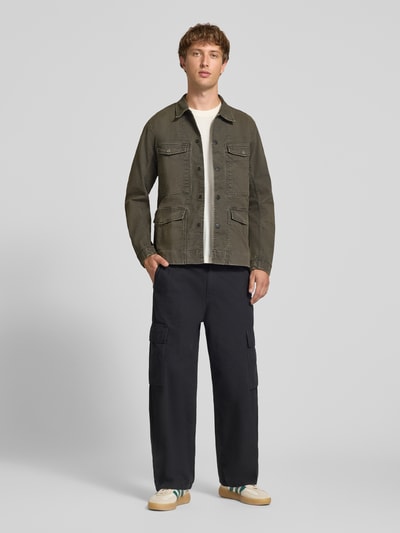 Männermodel trägt Slim Fit Jeansjacke aus reiner Baumwolle von G-Star RAW in Olivgrün, kombiniert mit dunkler Hose, Ganzkörperansicht von vorne.