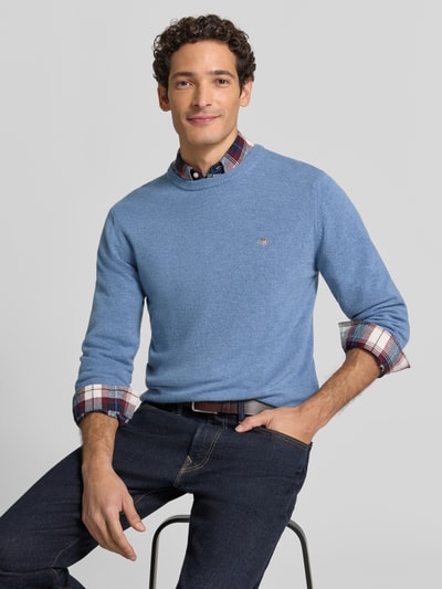 Mężczyzna nosi sweter Regular Fit Pullover aus reiner Wolle von GANT w jasnoniebieskim kolorze, widoczne faktury dzianiny, widok od przodu, zdjęcie całej sylwetki.
