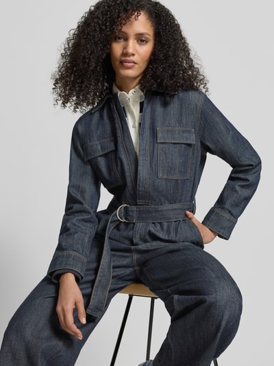 Frauenmodel trägt Jumpsuit mit kurzem Reißverschluss von Jake*s Casual in Denim-Optik, taillierter Schnitt, Stoffgürtel, Nahaufnahme Oberkörper.