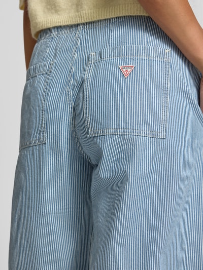 Frauenmodel trägt Jogger Pants mit Bindegürtel und Eingrifftaschen von Guess Jeans in hellblau-weißem Streifenmuster aus Baumwolle, Detailaufnahme Gesäßtaschen.