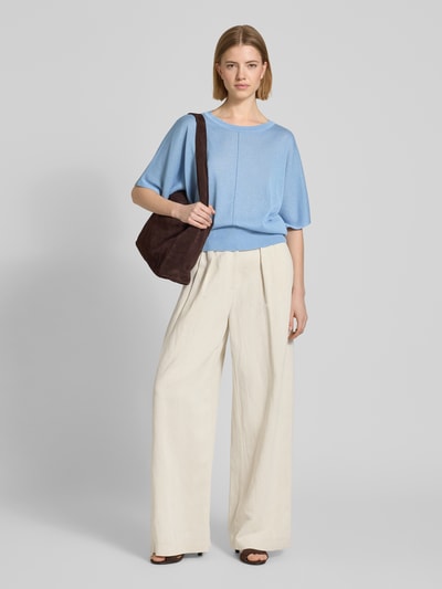 Frauenmodel trägt Relaxed Fit Oberteil aus Viskose-Mix in Strick-Optik von More & More in Hellblau, kombiniert mit weiter beigefarbener Hose, dezente Struktur, elastischer Bund, Rundhalsausschnitt, Halbarm, Ganzkörperansicht von vorne.
