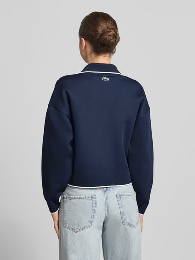 Frauenmodel trägt Regular Fit Sweatshirt mit Kontraststreifen von Lacoste in Optik: Unifarben, Passform: Regular-Fit, Polokragen, V-Ausschnitt, Langarm, Ärmelabschluss: Gerippt, Rumpfabschluss: Gerippt, dunkelblau mit weißen Details, glatte Textur, Ganzkörperansicht Rückansicht.