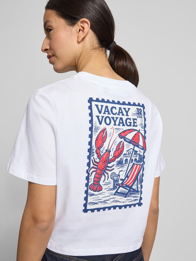 Frauenmodel trägt T-Shirt mit Knotendetail und Rundhalsausschnitt von Rich & Royal aus reiner Baumwolle in Weiß mit blau-rotem Print, Regular Fit, Rückenlänge bei Größe S 44 cm, Ganzkörperansicht Rückansicht.
