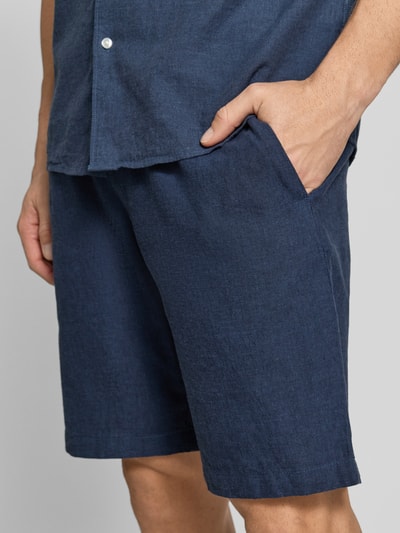 Męski model nosi Shorts aus Leinen-Baumwoll-Mix mit elastischem Bund od MCNEAL, kolor granatowy, krój regular fit, szerokość w rozmiarze M 44 cm, długość nogawki wewnętrznej 23 cm, widok z przodu, zbliżenie na górną część ciała.
