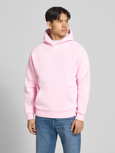 Männermodel trägt Hoodie mit Känguru-Tasche von REVIEW in Rosa aus Baumwollmischung, lockere Passform, Ganzkörperansicht von vorne.
