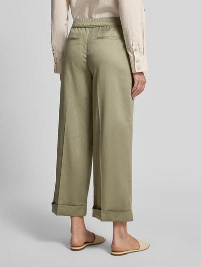 Männermodel trägt Wide Leg Pants mit Bindegürtel Modell 'Meeri bloom' von OPUS, zielonooliwkowy lyocell z bawełną, francuskie kieszenie, szerokość w rozmiarze 36: 40 cm, długość nogawki 68 cm, krój z rozszerzaną nogawką, widok całej sylwetki z tyłu.