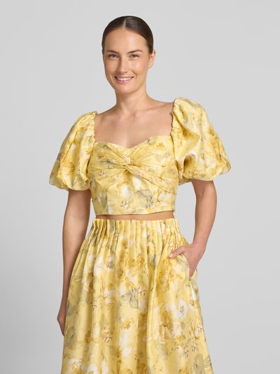 Frauenmodel trägt Cropped Blusentop mit Puffärmeln Modell 'LEMON' von YAS im gelben Allover-Look mit Knotendetail, Lyocell-Mix mit Leinen-Anteil, Ganzkörperansicht von vorne.