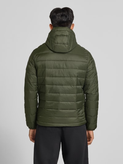 Męski model nosi Regular Fit kurtka z efektem pikowania Model 'KINGSLEY' od JACK & JONES w kolorze oliwkowym z kapturem, wpuszczane kieszenie, zamek błyskawiczny, długość tyłu w rozmiarze M: 70 cm, szerokość ramion w rozmiarze M: 45 cm, szerokość w rozmiarze M: 52 cm, długość rękawów w rozmiarze M: 67 cm, widok całej sylwetki od tyłu.
