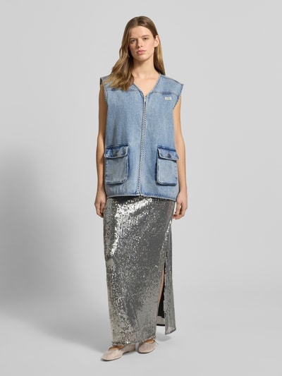 Frauenmodel trägt Jeansweste mit Label-Patch von Karo Kauer aus Reine Baumwolle im Loose-Fit, V-Ausschnitt, Reißverschluss, blaue Pattentaschen mit Knopfverschluss, kombiniert mit silbernem, glänzendem Rock, Ganzkörperansicht von vorne, Rückenlänge bei Größe S: 71 cm, Schulterbreite: 48 cm, Brustweite: 65 cm.