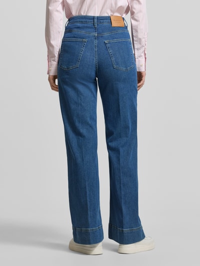 Kobiece modelka nosi Jeans mit seitlichen Knöpfen und Gesäßtaschen od Gant, mieszanka bawełny z dodatkiem streczu, krój regular fit, niebieski odcień, szerokość w rozmiarze 27: 35 cm, długość wewnętrzna nogawki 80 cm, widok całej sylwetki z tyłu.