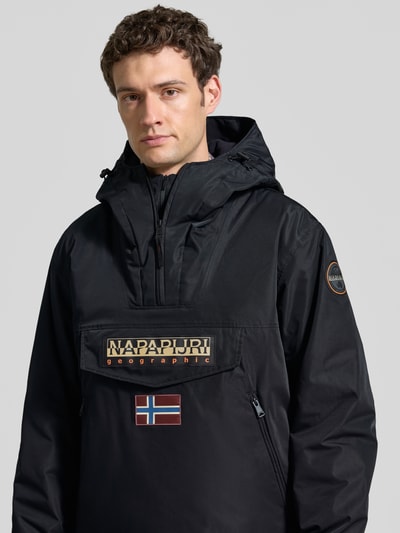 Mannenmodel draagt zwarte jack met capuchon en kort ritssluiting, labelpatches, Klepzak, recht model, Napapijri, Nahaufnahme Oberkörper. Heren jack 'Jacke mit Kapuze und kurzem Reißverschluss', Ruglengte maat M 73 cm, Schouderbreedte 53 cm, Borstwijdte 60 cm, Mouwlengte 64 cm.