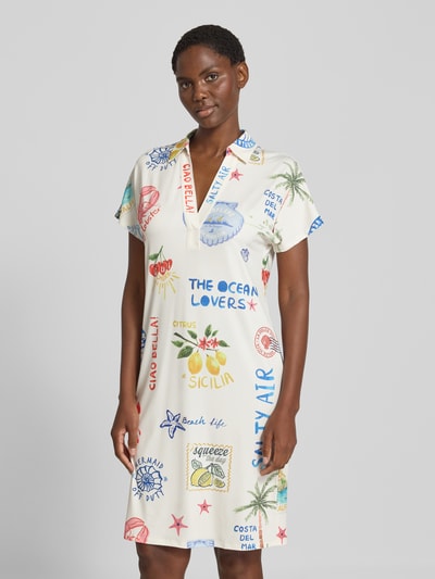 Frauenmodel trägt Regular Fit Kleid mit Allover-Motiv-Print von Oui in Weiß mit bunten Schriftzügen und Motiven, elastischer Material-Mix, Tunika-Kragen, kurzärmeliges Design, Ganzkörperansicht von vorne.