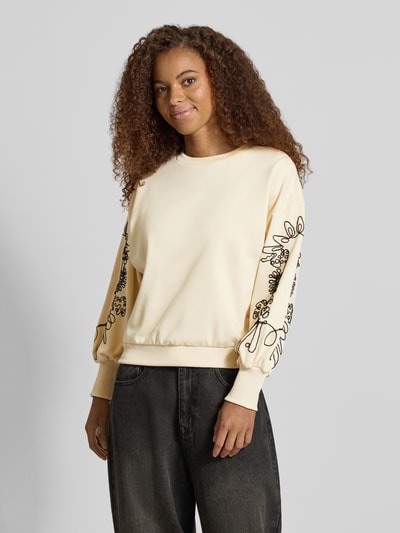 Kobieta modelka nosi Relaxed Fit Sweatshirt aus Baumwoll-Mix model 'BROOKE' od ONLY, kremowa bluza z czarnym haftem na rękawach, damska bluza od ONLY, zdjęcie całej sylwetki z przodu.