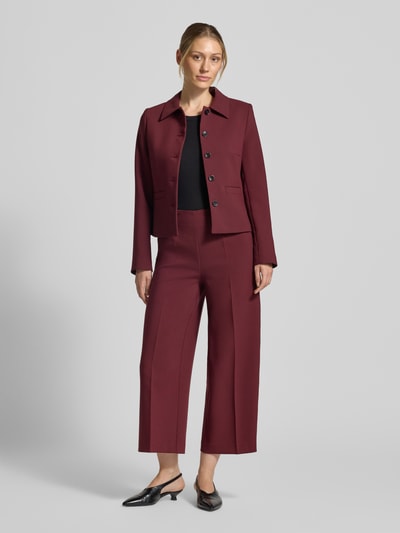 Frauenmodel trägt Stoffhose mit Bügelfalte und Eingrifftaschen von MORE & MORE in Bordeaux, glatte Textur, Ganzkörperansicht von vorne. Material-Mix mit Viskose-Anteil, Wide Leg Fit, seitlicher Nahtreißverschluss, französische Eingrifftaschen, Bundweite 35 cm, Innenbeinlänge 63 cm.