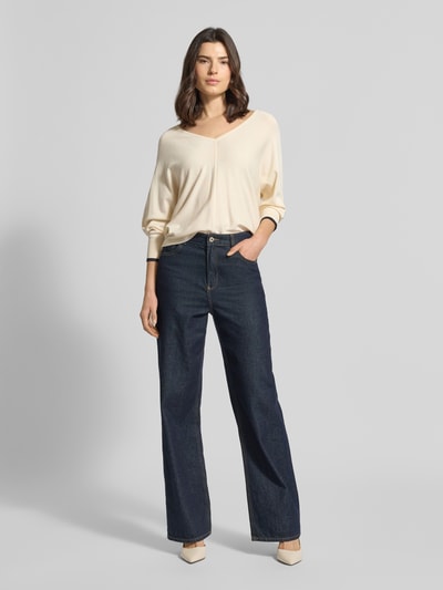 Modelka kobieca nosi Strickpullover aus Viskose-Mix mit V-Ausschnitt od comma, kremowy, krój regular fit, wykończenie rękawów z kontrastowym paskiem, długość tyłu 52 cm, długość rękawa 56 cm, widok całej sylwetki od przodu.