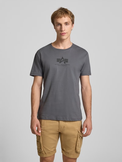 Männermodel trägt T-Shirt mit Logo und Rundhalsausschnitt von Alpha Industries in Grau, reine Baumwolle, Regular Fit, Ganzkörperansicht von vorne.