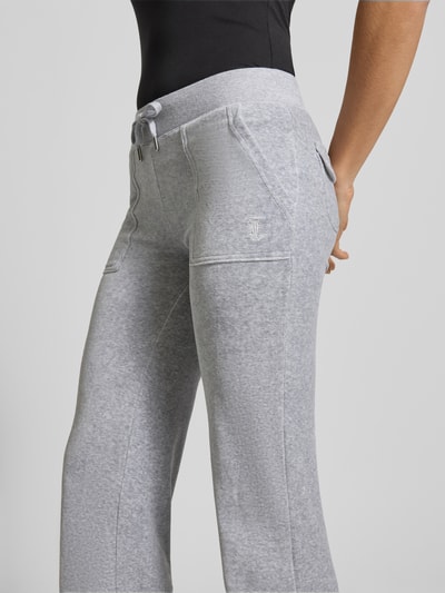 Frauenmodel trägt Low Rise Sweatpants mit elastischem Bund Modell 'LAYLA' von Juicy Couture, Baumwoll-Mix mit Stretch-Anteil, Flared-Cut, Eingrifftaschen, hellgraue Farbe, sichtbare Textur, Ganzkörperansicht Rückansicht.