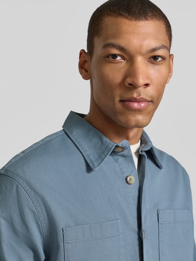 Mężczyzna nosi Regular Fit Hemdjacke aus Bio-Baumwoll-Mix Modell 'TRAVIS' od SELECTED HOMME, kolor jednolity, materiał twill, krój regular fit, kołnierz wykładany, zapinanie na guziki, długie rękawy z mankietami, kieszenie na piersi, perspektywa: zbliżenie na górną część ciała.