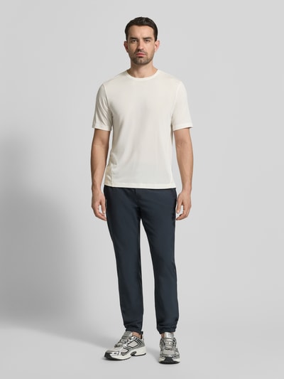 Männermodel trägt Funktionsshirt mit Rundhalsausschnitt und Logo von Salomon in Offwhite, glatte Textur, Ganzkörperansicht von vorne.