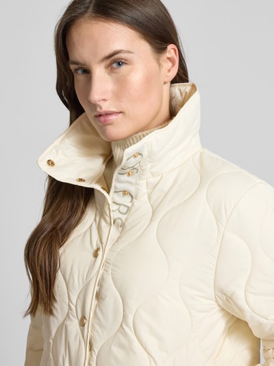 Kobiece model nosi Regular Fit Steppjacke mit gefüttertem Stehkragen od Christian Berg Woman Selection w kremowym kolorze, stepp-optik, kieszenie boczne, pełne zapięcie na guziki, szerokość w rozmiarze 36: 52 cm, długość tyłu: 62 cm, szerokość ramion: 41 cm, długość rękawa: 62 cm, zbliżenie na górną część ciała