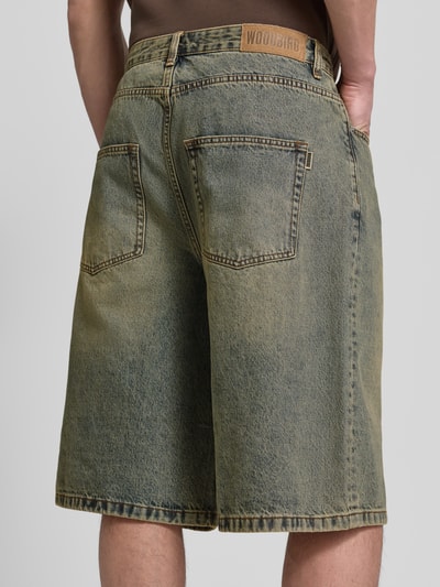 Männermodel trägt Jeansshorts mit Eingrifftaschen Modell 'Yuto Aged' von WOODBIRD aus reiner Baumwolle, Relaxed-Fit, Ganzkörperansicht Rückansicht. Bundweite 44 cm, Innenbeinlänge 33 cm bei Größe 32.