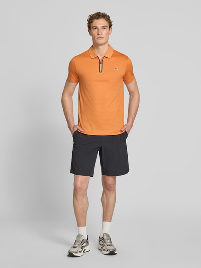 Männermodel trägt Slim Fit Poloshirt aus schnelltrocknendem Material von Lacoste, Optik: Unifarben, Logo-Patch, Ganzkörperansicht von vorne.