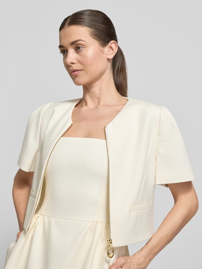 Frauenmodel trägt Slim Fit Kurzblazer mit Viskose-Anteil Modell 'Ambelle' von HUGO in Creme, Jacquard-Struktur, Nahaufnahme Oberkörper.