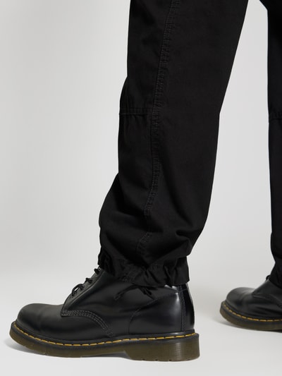 Männermodel trägt Straight Fit Cargohose mit Gesäßtaschen von G-Star Raw in Schwarz aus Baumwolle, Detailaufnahme Unterschenkel.