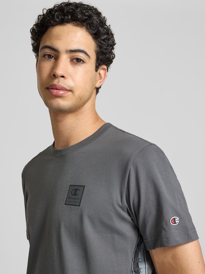 Männermodel trägt T-Shirt mit Logo und Rundhalsausschnitt von CHAMPION in Grau aus reiner Baumwolle, Regular Fit, Nahaufnahme Oberkörper.