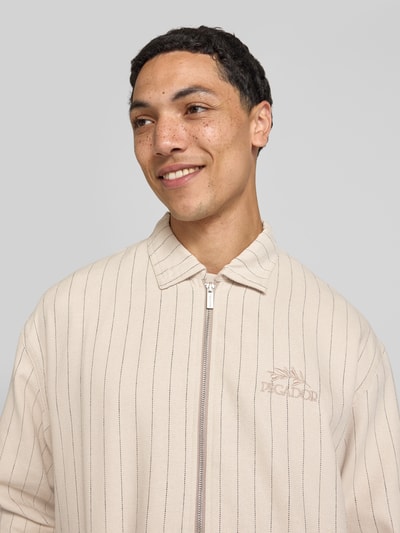 Mannelijk model draagt overshirt uit viscosemix met logostitching model 'Sistelo' van Pegador met kentkraag, relaxed fit, nahaufnahme bovenlichaam, heren, kleur beige met strepen, context heren overshirt Pegador, viscosemix met linnen, ritssluiting, ruglengte maat M 69 cm.