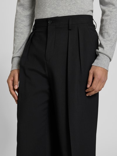 Männermodel trägt Wide Fit Stoffhose aus Woll-Mix von Filippa K in Schwarz mit Kellerfalten, Nahaufnahme Oberkörper.