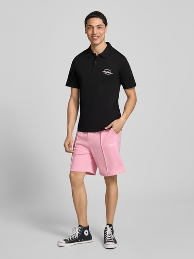 Männermodel trägt Poloshirt mit Label-Print Modell 'BRANDON' von Jack & Jones, Reine Baumwolle, Regular-Fit, Polokragen, kurze Knopfleiste, schwarze Farbe, Rückenlänge bei Größe M: 71 cm, Ganzkörperansicht von vorne.