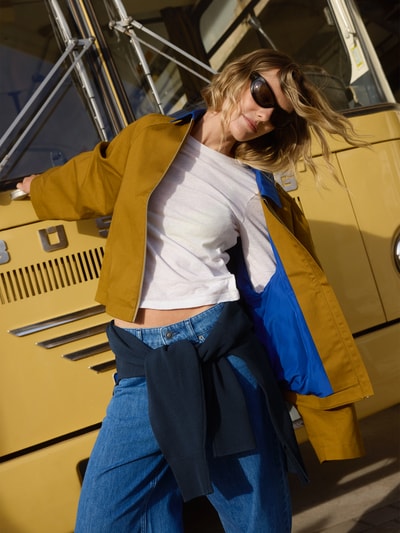 Modelka nosi Kurze Barn-Jacket mit Kontrast-Kragen - curated by Tinvcb od Tinvcb, musztardowa bawełna, krój relaxed fit, niebieska podszewka, kołnierz wykładany, zamek błyskawiczny, długość tyłu w rozmiarze 36: 56 cm, szerokość ramion w rozmiarze 36: 44 cm, szerokość w biuście w rozmiarze 36: 60 cm, długość rękawa w rozmiarze 36: 57 cm, całkowity widok z przodu