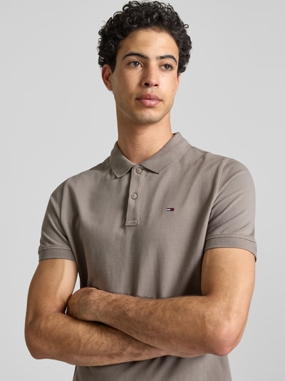 Männermodel trägt Regular Fit Poloshirt Modell 'TJM SLIM PLACKET POLO EXT' von Tommy Jeans in Unifarbe mit Logo Stitching und Polokragen, Nahaufnahme Oberkörper.