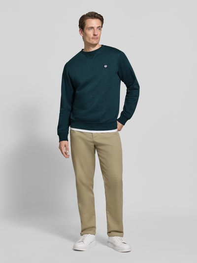 Männermodel trägt Regular Fit Sweatshirt aus Baumwoll-Mix von LERROS in Dunkelgrün mit Logo-Patch, Rundhalsausschnitt, Ganzkörperansicht von vorne.