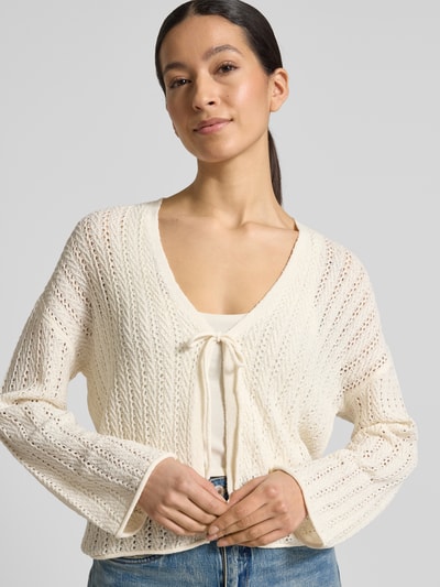 Modelka nosi Regular Fit Strickjacke mit Lochstrickmuster von Tom Tailor Denim w kolorze kremowym, wzór ażurowy, detal wiązania, widok przód, zbliżenie na górę ciała.