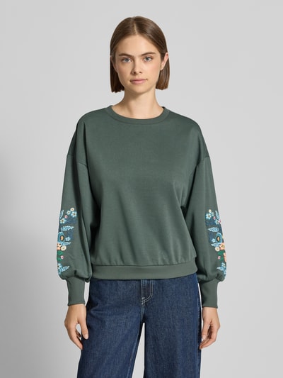 Frauenmodel trägt Relaxed Fit Sweatshirt aus reiner Baumwoll-Mix Modell 'BROOKE' von ONLY, dunkelgrün mit Blumenstickerei, Damen Sweatshirt, Ganzkörperansicht von vorne.