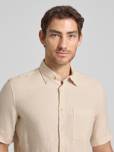 Mężczyzna nosi Regular Fit Freizeithemd aus reinem Leinen von Marc O'Polo w kolorze jasnobeżowym, flammgarn, krój regular fit, krótki rękaw, kieszeń na piersi, kent kołnierzyk, materiał czysty len, gładka faktura, zapięcie na guziki. Zbliżenie górnej części ciała z przodu.