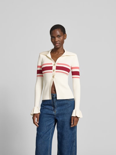 Frauenmodel trägt Strickjacke aus Viskose-Mix von Self-Portrait in Creme mit roten Streifen, Umlegekragen, geraffte Ärmelabschlüsse, Knopfleiste, eng anliegende Passform, Rückenlänge 55 cm, Brustweite 38 cm, Ärmellänge 68 cm, Ganzkörperansicht von vorne.