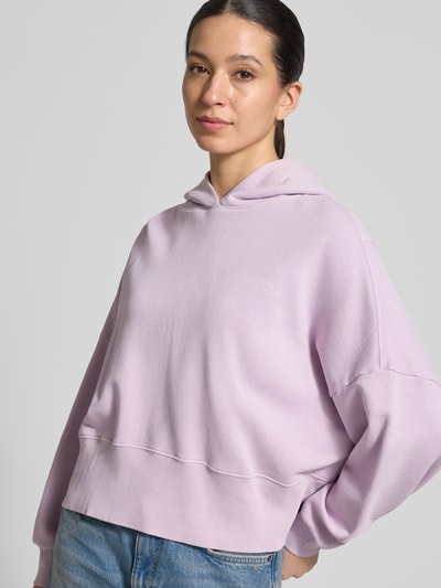 Frauenmodel trägt Relaxed Fit Hoodie aus reiner Baumwolle von Marc O'Polo, Optik: Unifarben, Applikation: Label-Print, Materialverarbeitung: Sweat, Farbe: Helllila, überschnittene Schultern, Kapuze, Langarm, Ärmelabschluss und Rumpfabschluss: Gerippt, Ganzkörperansicht von vorne.