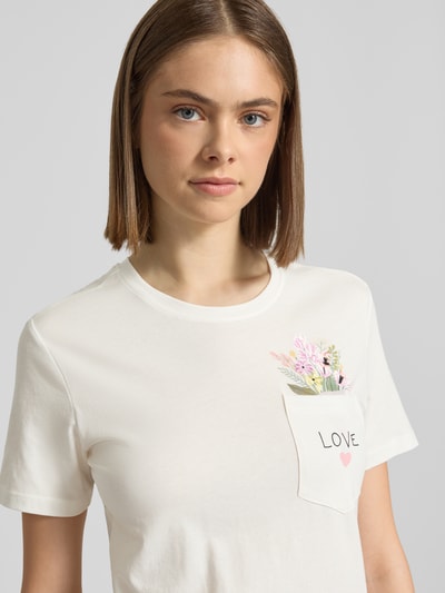 Frauenmodel trägt Regular Fit T-Shirt aus reiner Bio-Baumwolle Modell 'POLLY' von Only, Optik: Unifarben, Jersey, Statement-Print-Applikation, Kurzarm, Brusttasche mit Motiv-Stitching, Nahaufnahme Oberkörper.